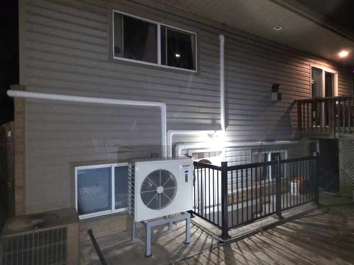 Heat pump outdoor unit installed on a stand beside a house